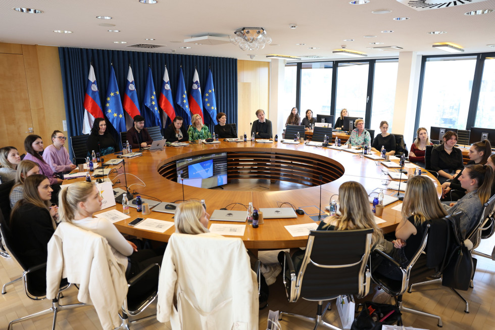 Za okroglo mizo sedijo študentke, v ozadju so slovenske in evropske zastave.