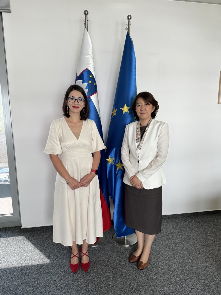Ministrica in veleposlanica stojita pred slovensko in evropsko zastavo
