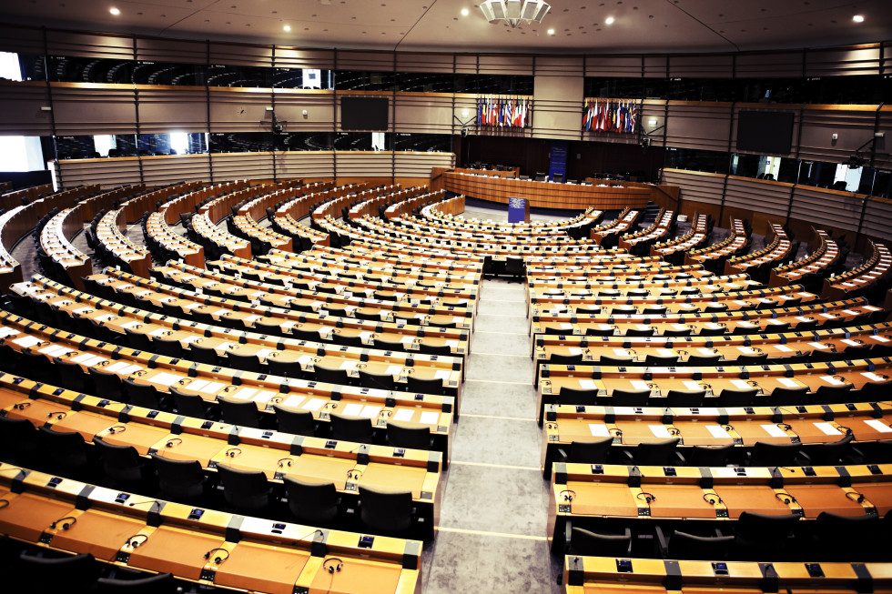 Prazna dvorana evropskega parlamenta, kjer so v krogu ena za drugo nanizani mize in stoli.