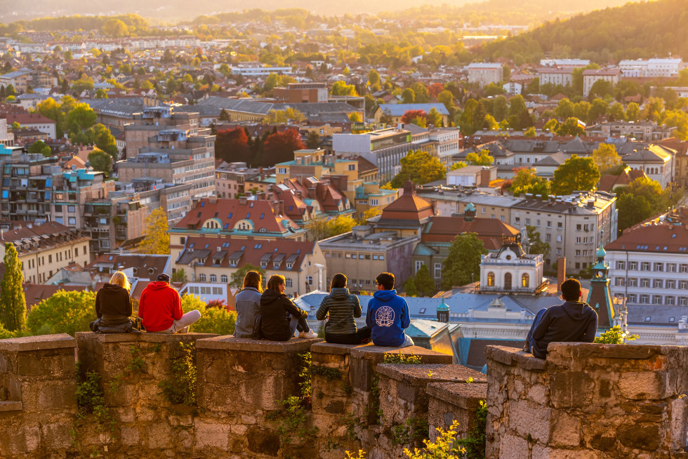 Na obzidju ljubljanskega gradu sedijo mladi in opazujejo razgled na Ljubljano.