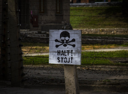 Znak na lesenem drogu, na njem lobanja s prekrižanimi kostmi in z napisom Halt! Stoj!. Za drogom žičnata ograja. 