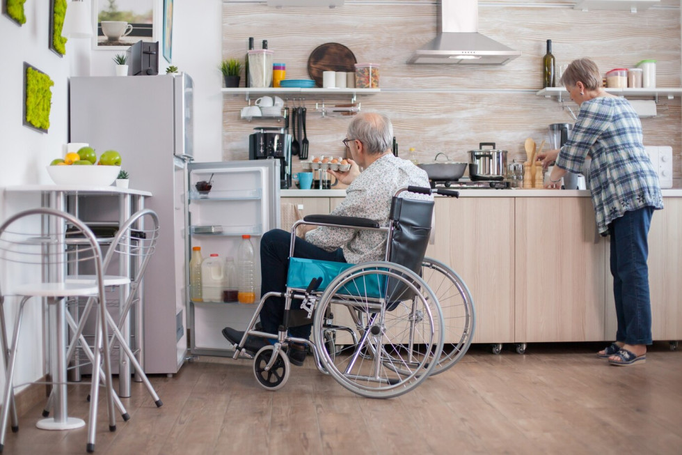 Starejši moški na vozičku z ženo v kuhinji