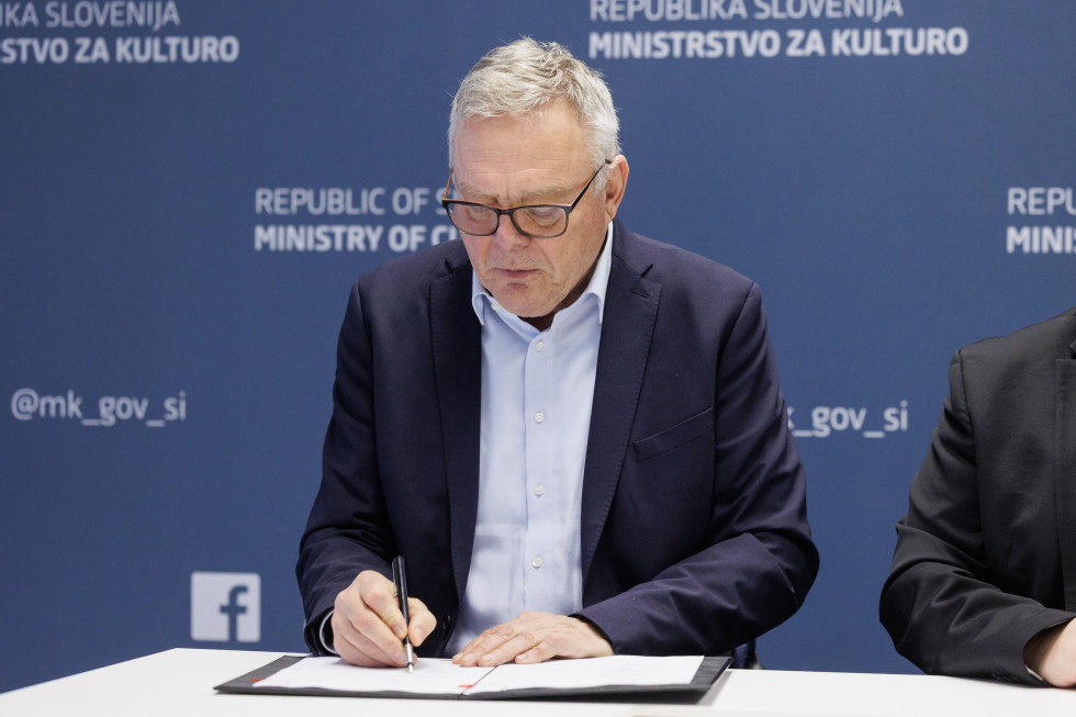 Minister Jože Novak sedi za mizo in podpisuje dokument s programo obnove kulturnih spomenikov