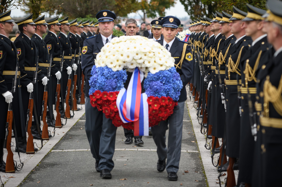 Policista neseta venec k spomeniku na Žalah, v ozadju častna garda Slovenske vojske