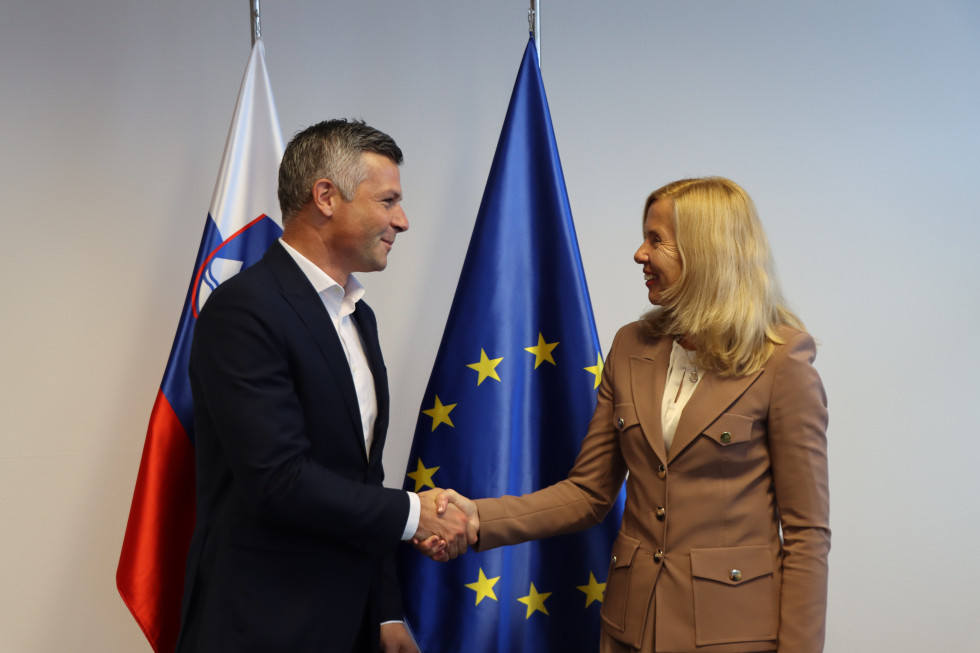 Ministrica Tatjana Bobnar se rokuje z evropskim poslancem Matjažem Nemcem; za njima sta slovenska in evropska zastava.