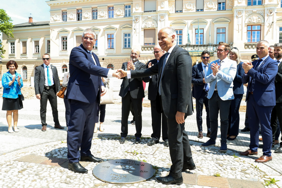 Ministra stojita na Trgu Evrope v Novi Gorici. Na tleh med njima je krog, ministra stojita en nasproti drugega okoli tega kroga in se rokujeta.