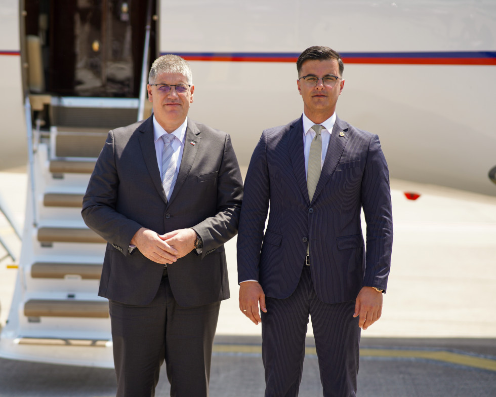 Slovenian and Montenegrin Ministers of the Interior Boštjan Poklukar and Danilo Šaranović stand side by side, with a white plane behind them