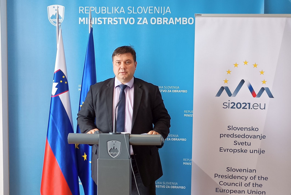 Direktor za govornico pred zastavama Slovenije in EU ter panojem predsedovanja Slovenije Svetu EU