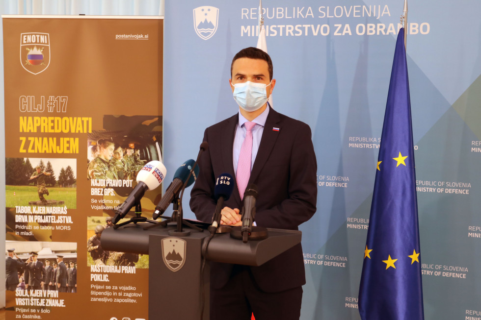 Minister Tonin na novinarski konferenci za govornico, pred panojem MORS in plakatom promocije SV, Enotni