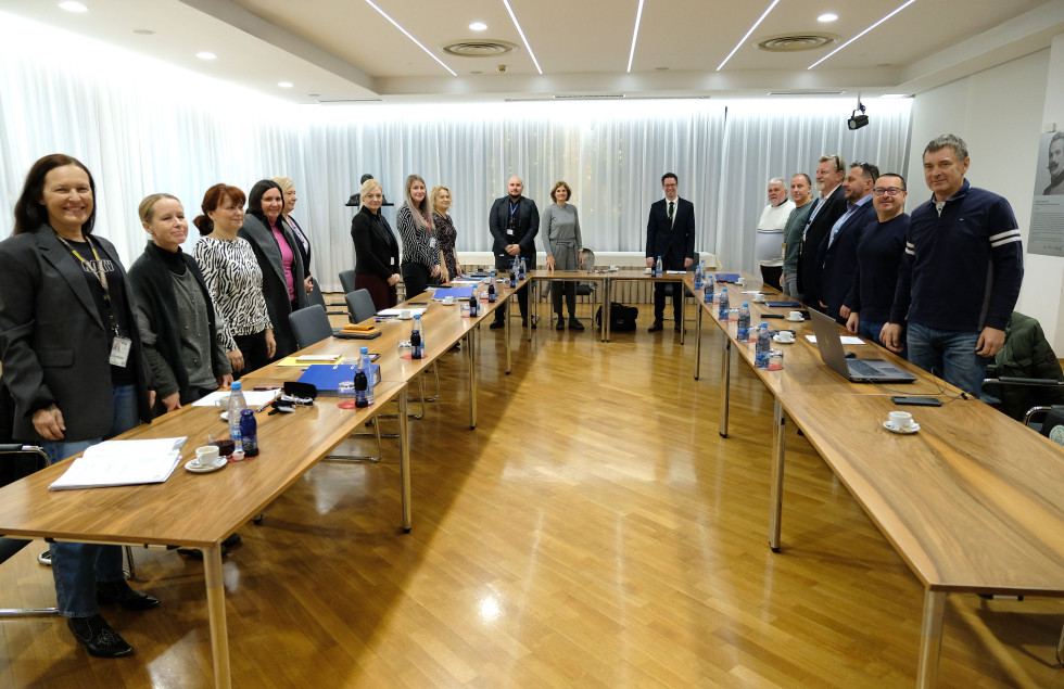 Udeleženci pogajanj stojijo za konferenčnimi mizami v dvorani