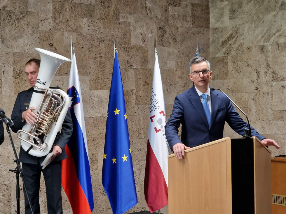 Minister med govorom stoji za govornico. Za njim so zastave EU, Slovenije in občine Kranj
