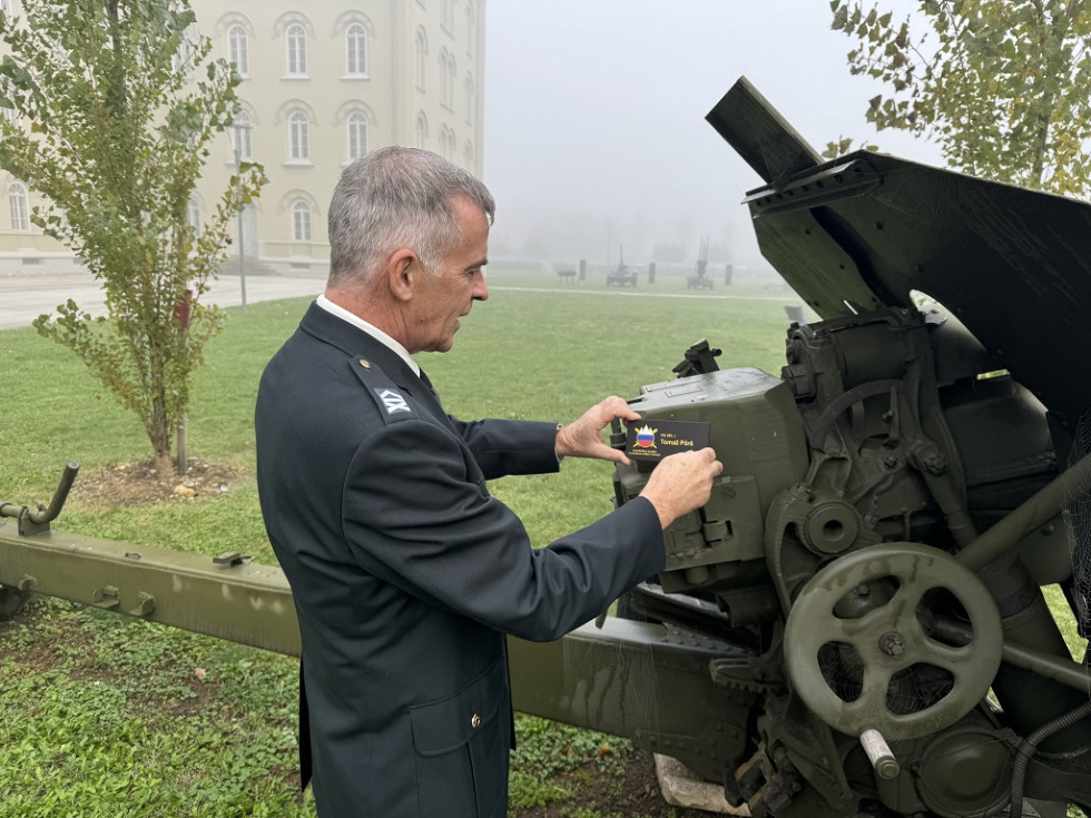 Vojaški uslužbenec Pörš pripenja tablico botrstva na muzejski predmet, ki je razstavljen na zelenici pred mariborsko Kadetnico.