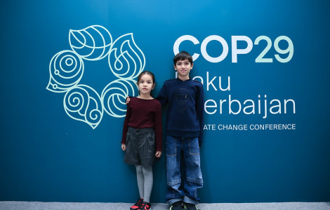 COP29 (Deklica in deček stojita pred panojem COP29)