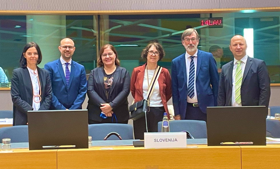 Delegacija skupaj z ministrom stoji v dvorani zasedanja v Bruslju