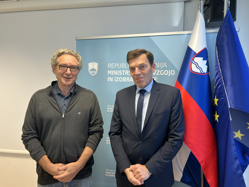 Dr. Vinko Logaj in Branimir Štrukelj stojita pred panojem Ministrstva za vzgojo in izobraževanje.