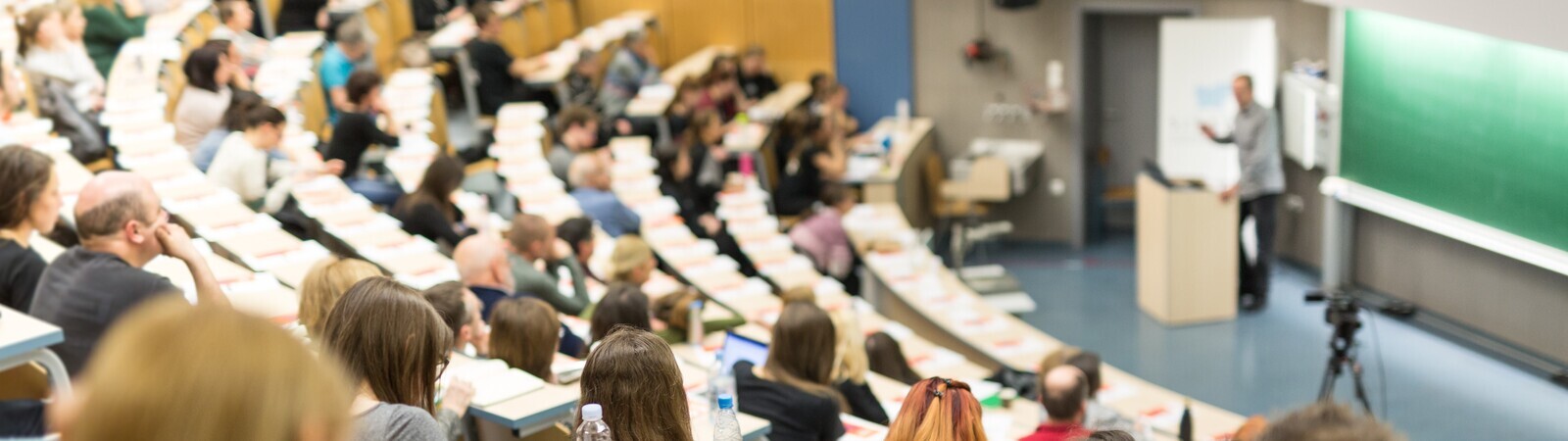 Študentke in študenti v predavalnici, v ozadju profesor za katedro.