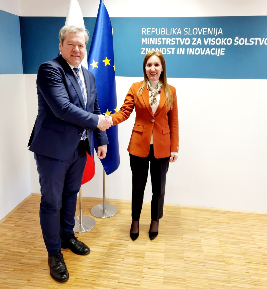 Minister Papič med rokovanje z veleposlanico Sabrino Kaci Bey, v ozadju slovenska in evropska zastava.