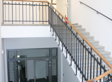 Curved staircase with a combination of granite floor, historic metal handrail and wood handrail. 