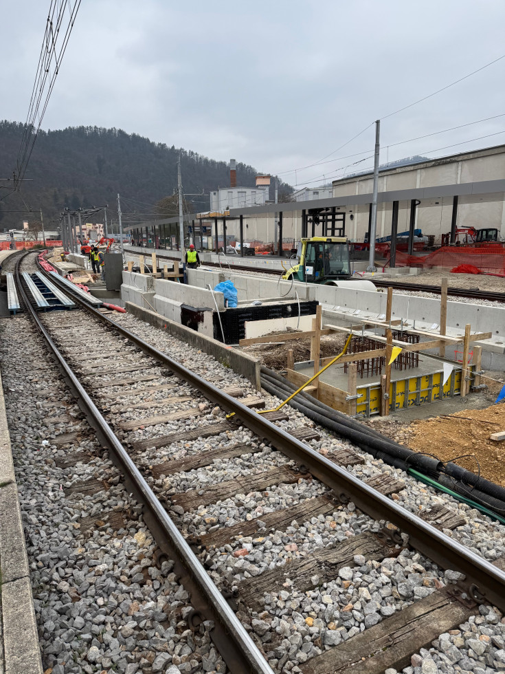 Pogled na tire in ob njih na betonsko konstrukcijo stopnišč. V ozadju peron št. 2.