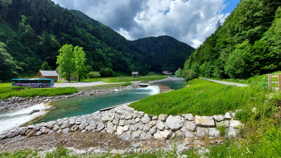 Ozelenela pokrajina, sredi slike reka, v ozadju cesta z avtobusom