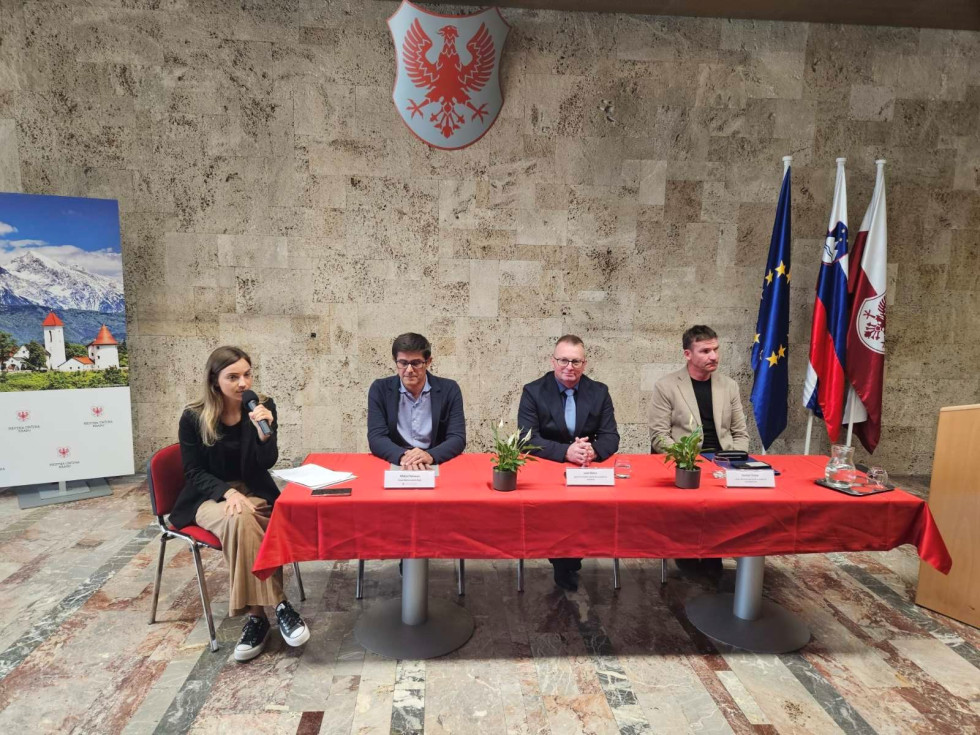 štiri osebe sedijo za govorniško mizo v ozadju zastave Slovenije, Evropske unije, Mestne občine Kranj in grb Mestne občine Kranj