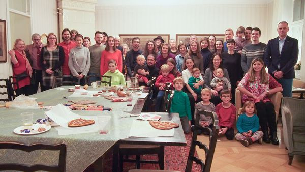 members of the society, some standing in the background, others sitting in front of them, right in the front of the picture a table with cookies