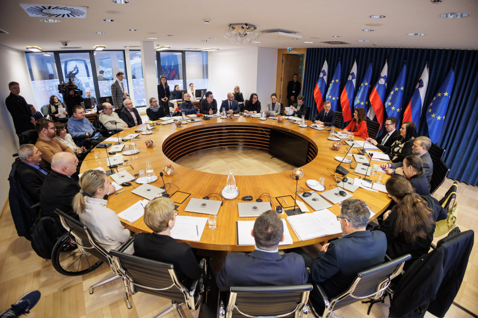 The prime minister and representatives of disabled persons' organisations sit at the round table. On the side are the Slovenian and EU flags.