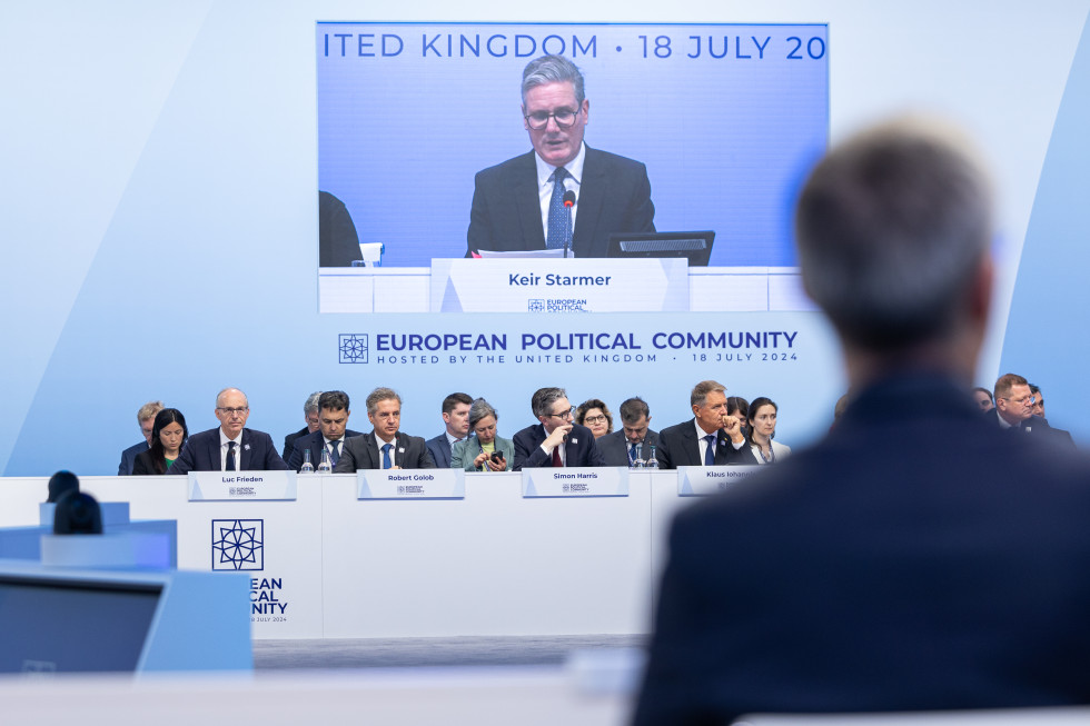 Udeleženci vrha Evropske politične skupnosti sedijo za omizjem. V ozadju slika govora predsednika vlade Združenega kraljestva Velike Britanije in Severne Irske Keir Starmerja.
