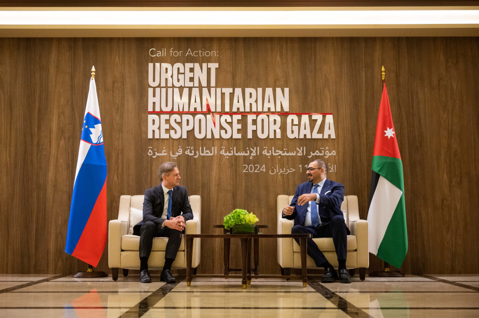 Premier Golob in državni minsiter Al-Jazijem sedita na foteljih in se pogovarjata, ob njunih straneh slovenska in jordanska zastava