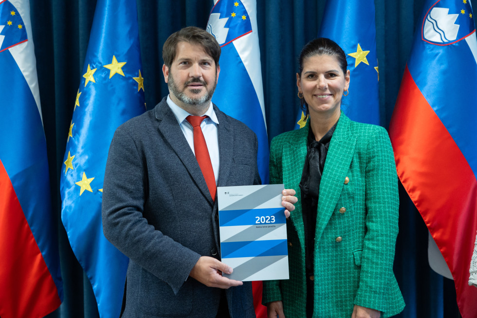 Miha Lobnik in Nataša Lužar stojita ob zastavah s poročilom v roki