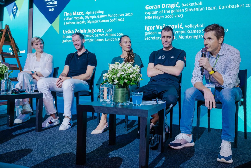 Urška Žolnir Jugovar, Goran Dragić, Tina Maze, Igor Vušurović in Andraž Vehovar sedijo na odru, pred njimi je miza s cvetjem. Vehovar govori v mikrofon, ki ga drži v roki.