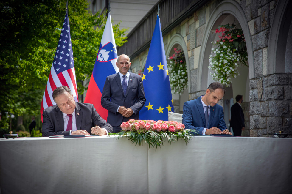 oba ministra podpisujeta sporazum v zunanjosti Vile Bled, za njima predsednik slovenske vlade