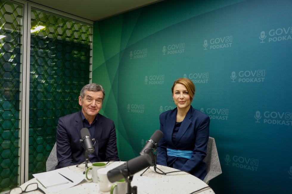 A man and a woman sitting at a desk with microphones.