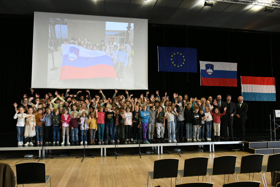 Otroci na Evropski šoli v Luksemburgu, v ozadju slovenska, evropska in luksemburška zastava.