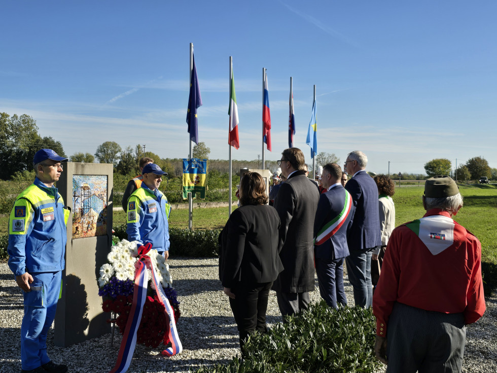 Državna sekretarka, generalni konzul in drugi prisotni na spominski slovenosti. Pred spomenikom, v ozadju zastave.