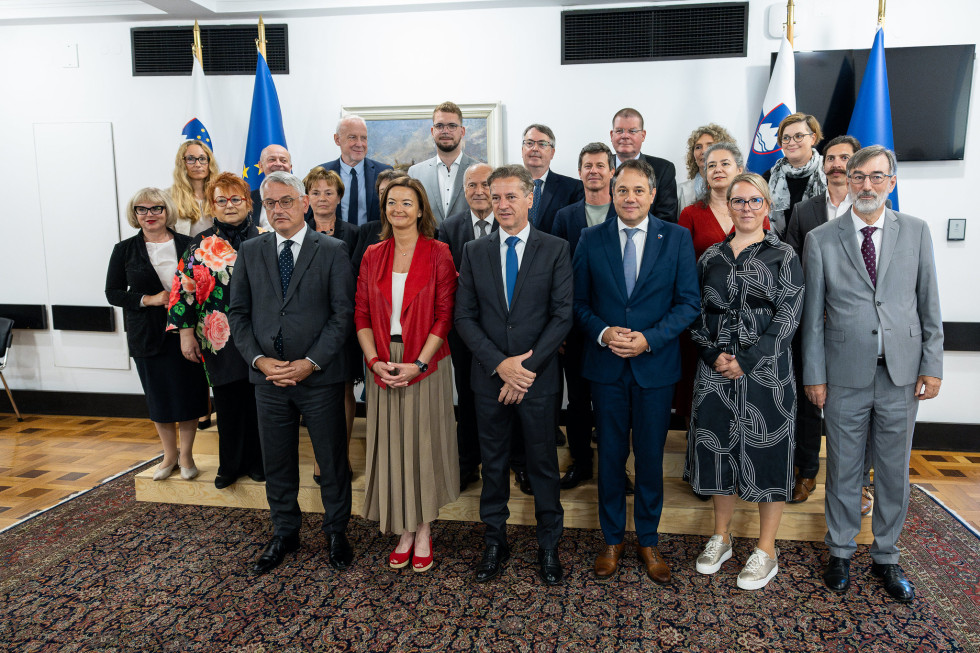 Premier, minister Arčon in drugi ministri ter ostali člani sveta vlade stojijo pred zastavami.